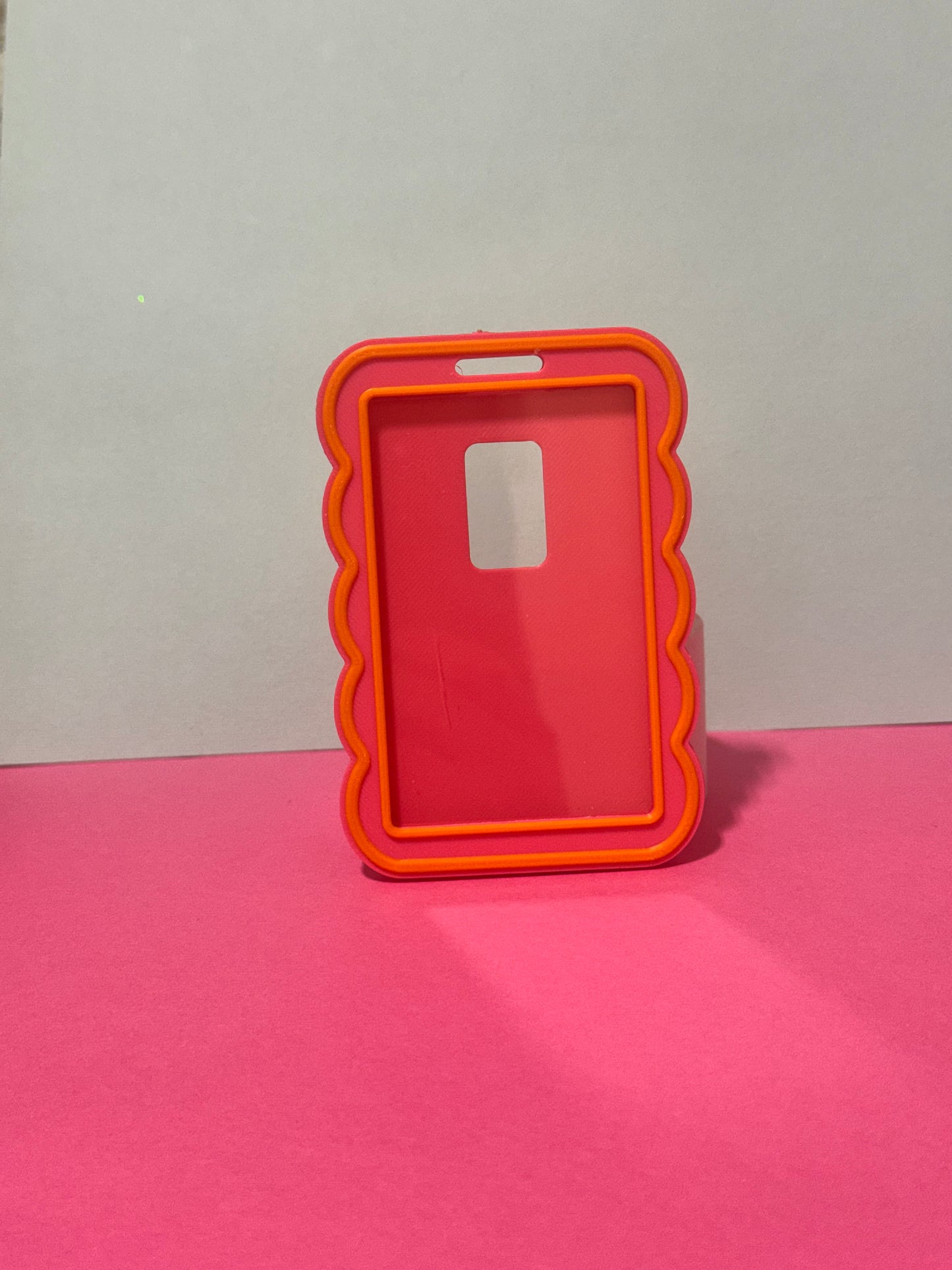 A translucent red phone case with a bright orange scalloped border, standing upright on a pink surface against a light gray background.