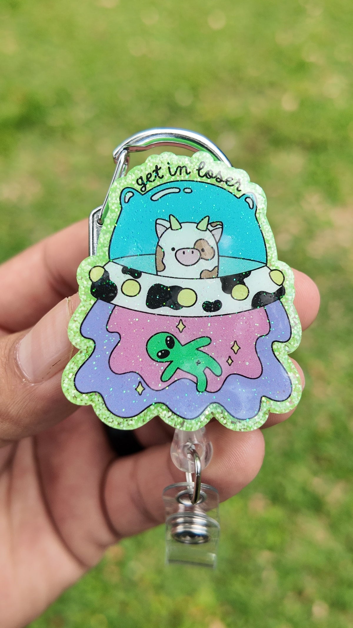 Colorful alien UFO badge reel with cow abduction, green alien and Get in Loser lettering