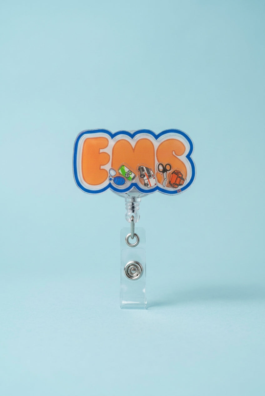 EMS shaker badge reel with orange lettering, a blue border, and miniature ambulance, trauma shears, emergency bag, and medical accessories.