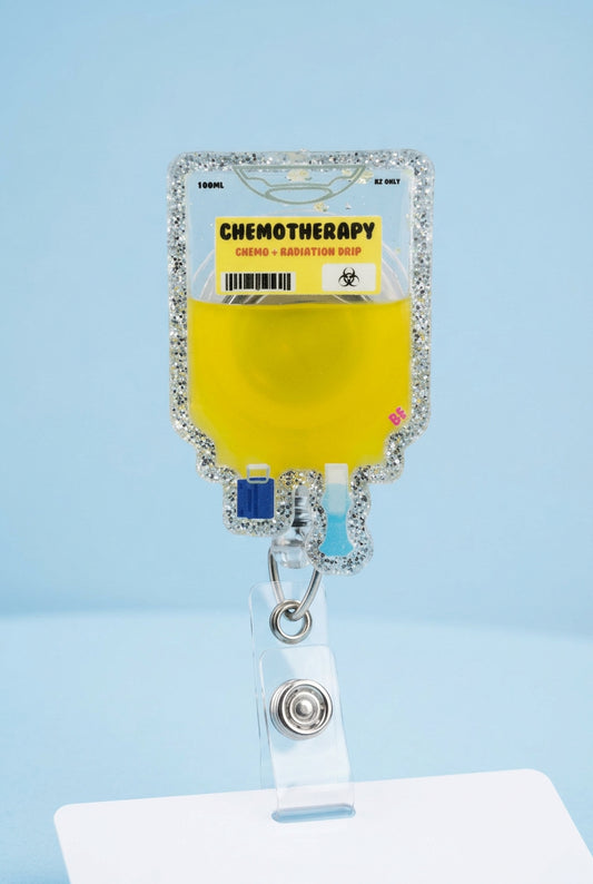A novelty chemotherapy-themed keychain bag held by a hand wearing a pink glove, set against a blurred outdoor background.