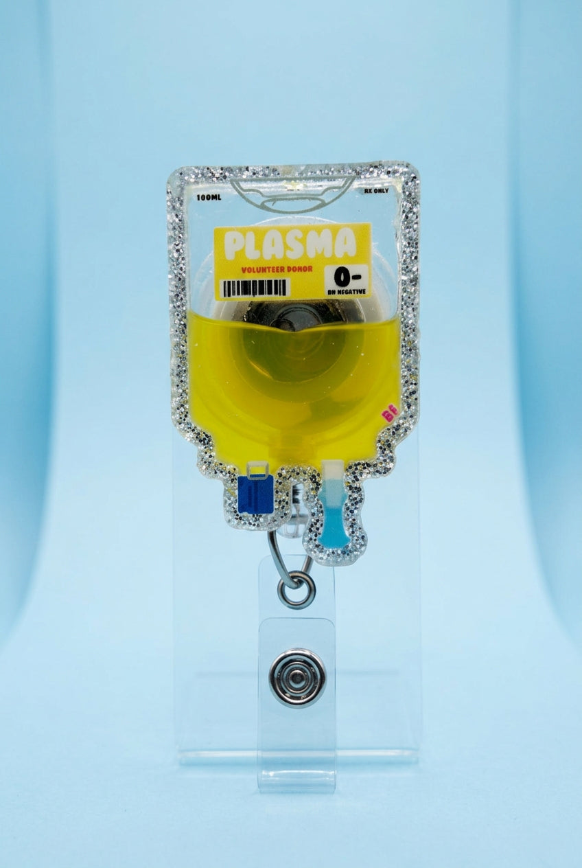 A novelty IV bag keychain or ID holder shaped like a glittery 'Plasma' bag filled with yellow liquid, held by a hand wearing a pink glove on a wooden deck.