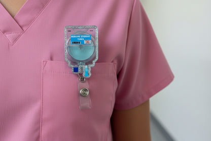 Hand holding a badge reel with 'Nursing Student Tears' text against a plain background