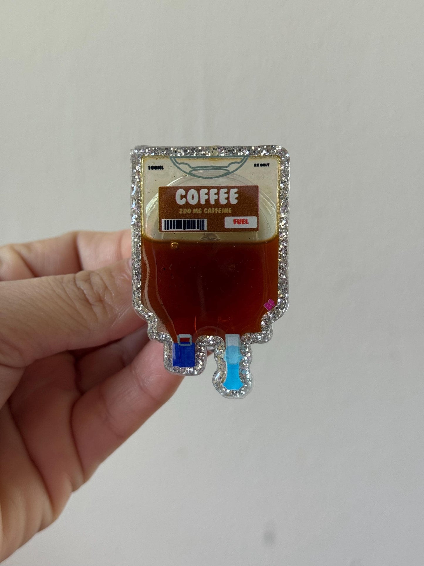 Hand holding a novelty coffee bag shaped like a medical IV bag on a plain background